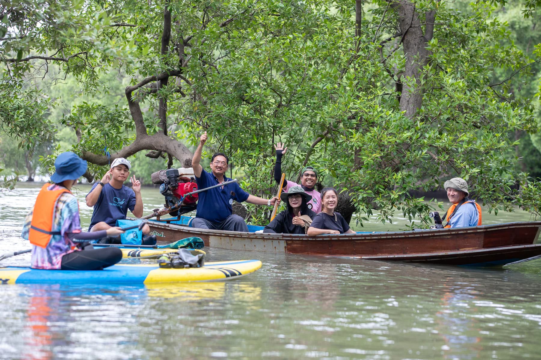 คนในพื้นที่และผู้มาเยือนโบกมือทักทายกันจากเรือในคลองป่าชายเลน