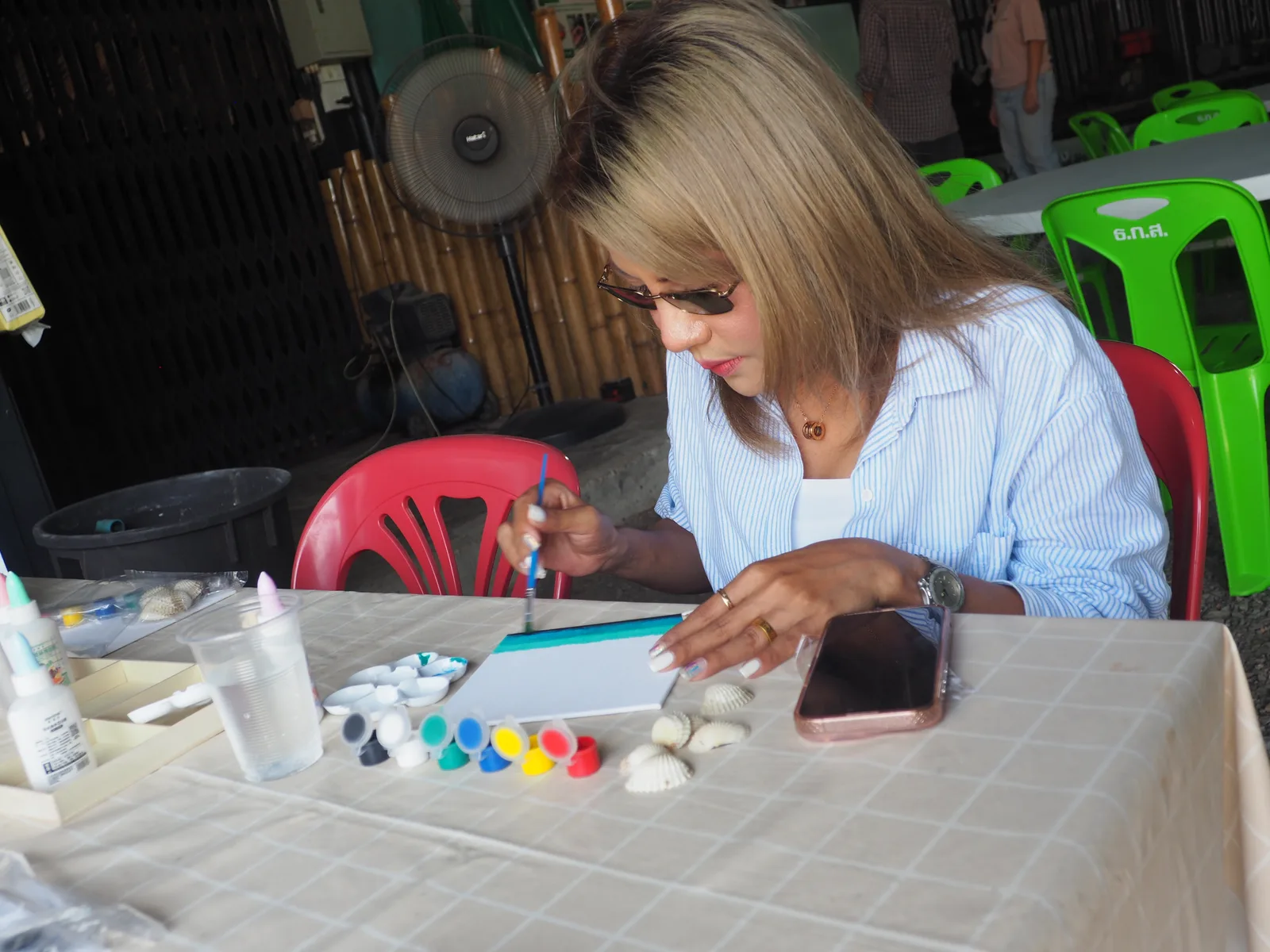 A guest painting a craft piece with shells and brushes on the table